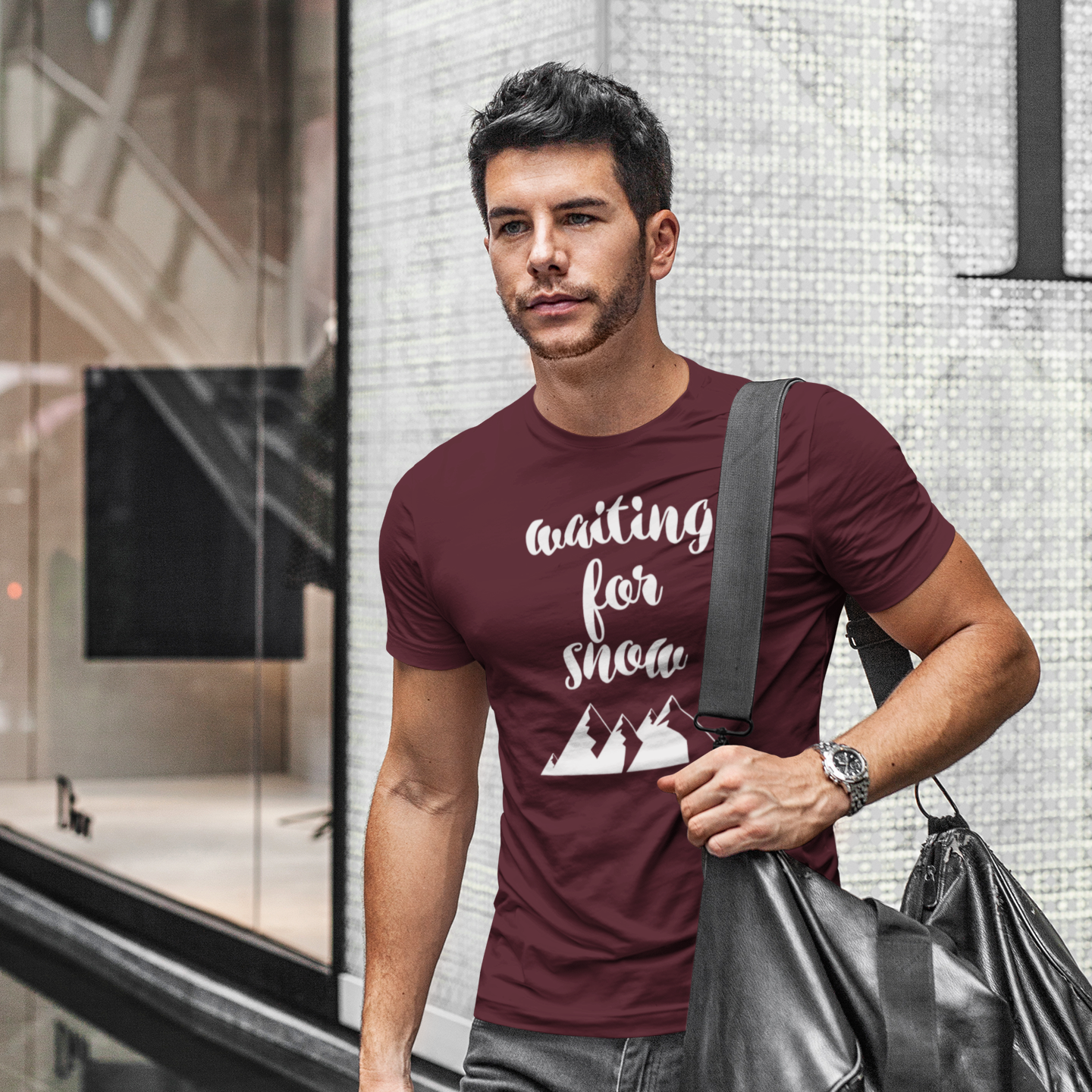 Man walking in city holding bag wearing burgundy shirt with 'Waiting for snow' print by KMLeon.