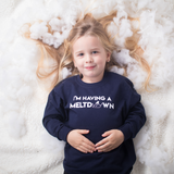 Blonde girl laying on snow with hair spread out, wearing navy shirt with 'I'm having a meltdown' print by KMLeon.