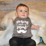 Toddler boy wearing mocha shirt, with 'Staching through the snow' print by KMLeon, leaning against rug.