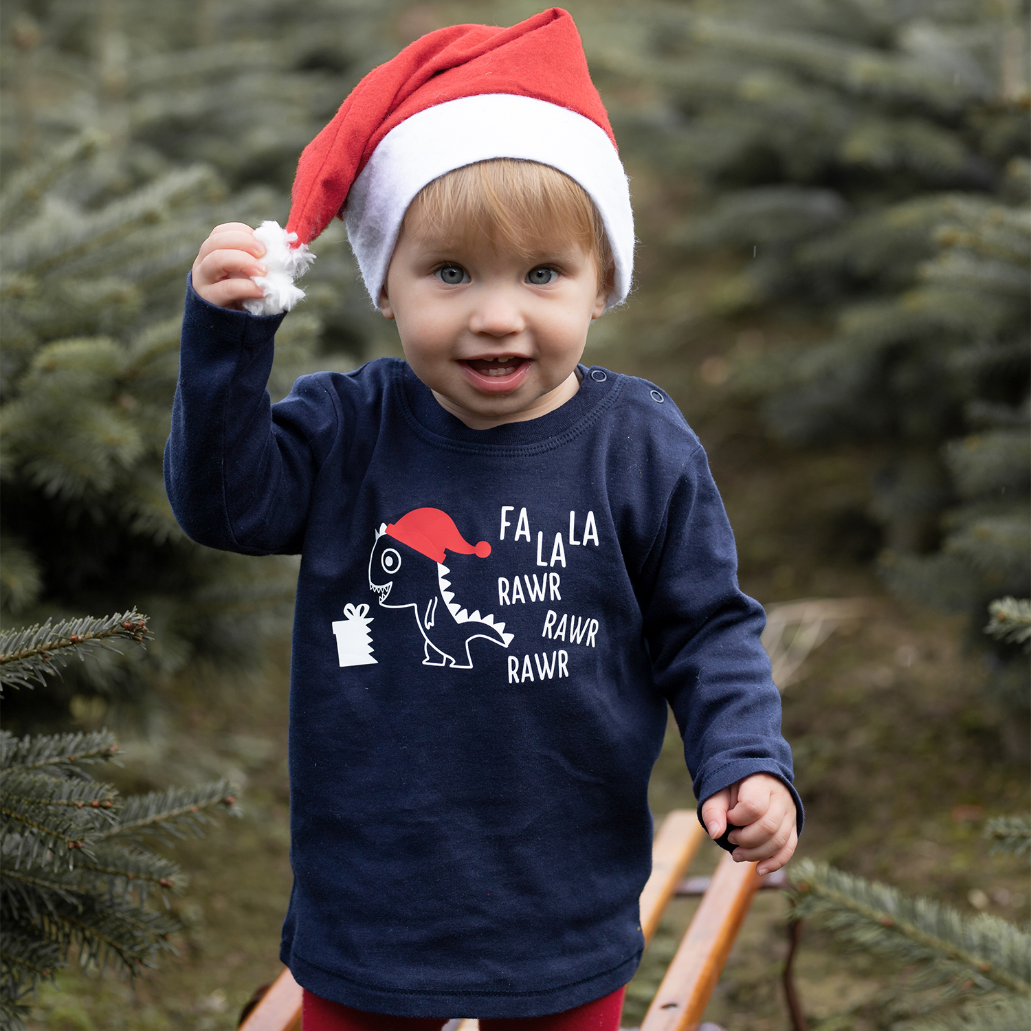 Blonde girl with christmas hat, wearing navy shirt with long sleeves with dino 'Fla La La Rawr Rawr Rawr' print by KMLeon.