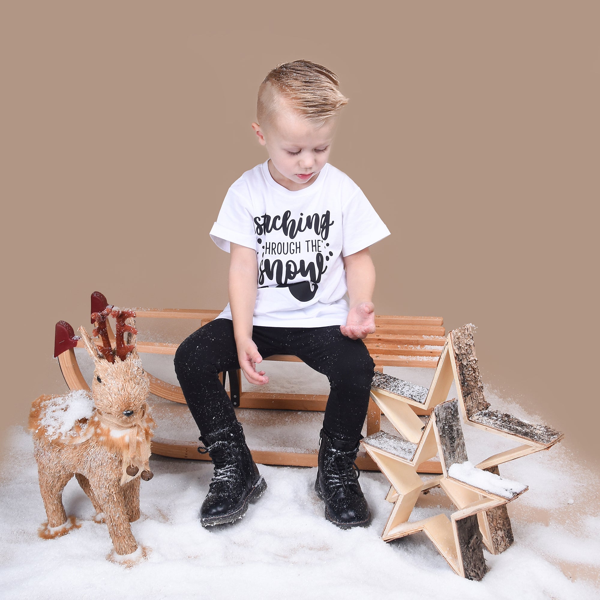 Blonde boy playing with snow, wearing white shirt with 'Staching through the snow' print by KMLeon.