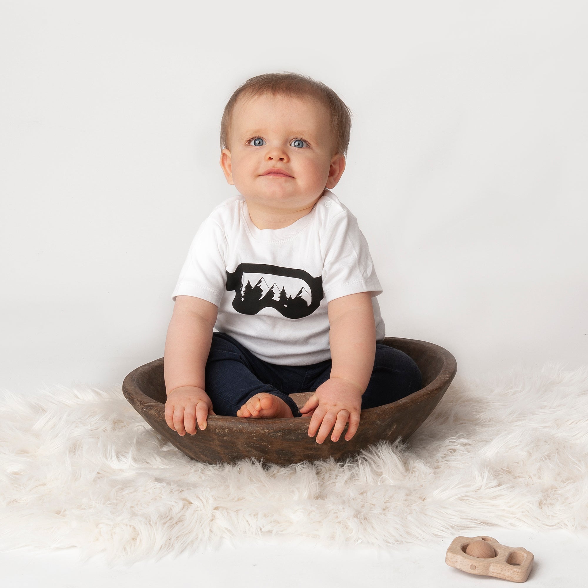 Little boy wearing white shirt with ski goggles print by KMLeon sitting in brown dish.